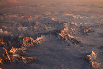 Sunset over Italian Alps. Aerial photo with the amazing mountain peaks covered with snow from Alps Mountains and sea of clouds between them. Nature landscape with mountains in sunset light.