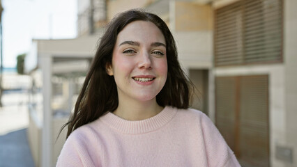 Portrait of an attractive, young caucasian woman smiling outdoors on a sunny urban street.