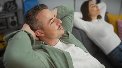 A relaxed man and woman rest on a couch at home, embodying casual comfort and domestic tranquility.