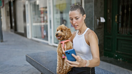 Young caucasian woman with dog using smartphone sitting on a bench at street