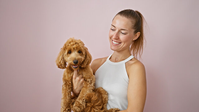Young caucasian woman with dog smiling hugging over isolated pink background