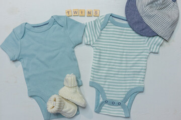 Flat lay of two blue baby boy onesies with booties and cap, Twins word on white background with copy space for gender reveal and twin boys announcement