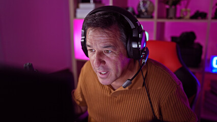 Mature man gaming in a dark room with purple lighting focused on screen