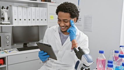 A smiling young man in lab coat using tablet in modern laboratory setting.