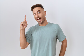 Hispanic man with beard standing over white background pointing finger up with successful idea. exited and happy. number one.