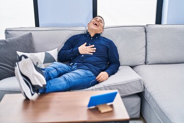 Fototapeta premium Young latin man watching movie on touchpad sitting on sofa at home