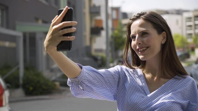 A beautiful young Caucasian woman takes selfies with a smartphone in a street in an urban area
