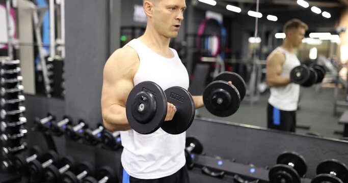Male athlete lifting dumbbells and training arm muscles in gym 4k movie slow motion. Sports training and healthy lifestyle concept