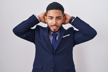 Young hispanic man wearing business suit and tie relaxing and stretching, arms and hands behind head and neck smiling happy