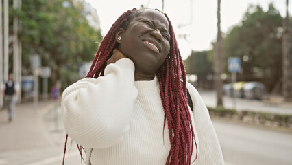 African american woman with braids expressing neck pain outdoors in an urban street setting.