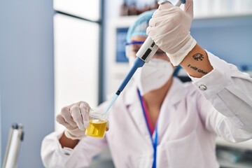 Young beautiful hispanic woman scientist pouring liquid to urine test tube at pharmacy