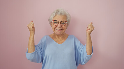 Cheerful senior woman with grey hair celebrating victory isolated on a pink background