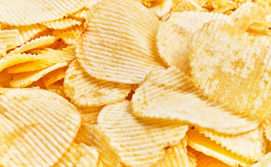 Close-up of golden crispy potato chips textured background with ridges, ideal for food and snack themes.