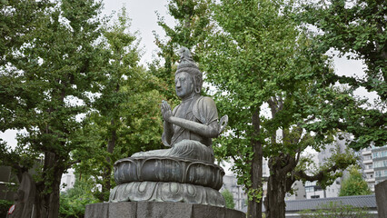 Serene buddha statue meditating among trees in a peaceful asian temple setting with buildings in the background.