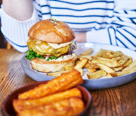 Woman enjoying a gourmet burger with fries and sweet potato fries in a casual dining setting.