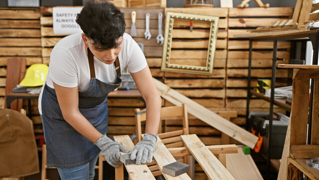 A young adult man is sanding wood in a well-organized carpentry workshop, showcasing craftsmanship and manual labor.