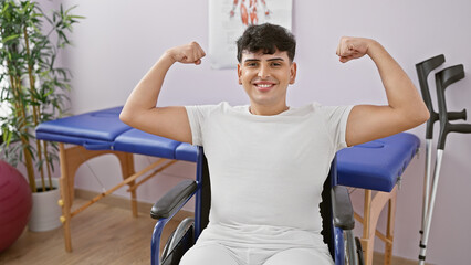 Fototapeta na wymiar A smiling young man in a wheelchair flexing muscles confidently in a rehab clinic's bright room.