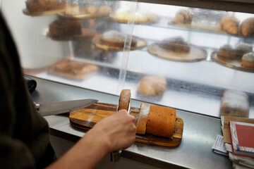 Hands cutting a bun on a table next to a glass display case