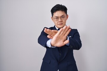 Young asian man wearing business suit and tie rejection expression crossing arms and palms doing...