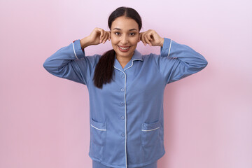 Young arab woman wearing blue pajama smiling pulling ears with fingers, funny gesture. audition...