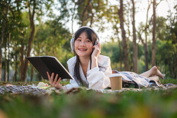Pretty young woman listening to music in headphone and reading book in the park.