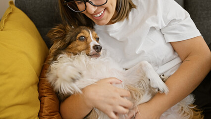 Hispanic woman cuddling with dog in a cozy living room setting, depicting friendship and comfort.