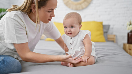 Casual indoor lifestyle of a lovely mother and daughter, together sitting on bed, looking at each other with cool expression in their apartment bedroom, amid a beautiful family relationship.