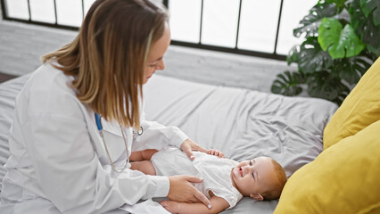 Obraz premium Confident female doctor joyfully examining adorable baby, sitting on bed in cozy bedroom - casual healthcare moment in a loving home environment