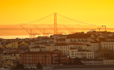 25 April Bridge and Port of Lisbon. Sunset photo in Lisbon, view to this landmark bridge and the cranes in the shipping cargo port. Travel to Portugal.