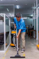 A middle aged janitor cleans the concrete floor with a professional wet and dry vacuum cleaner.