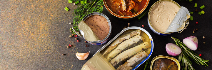 Different open tin cans with canned fish among spices and herbs banner, canned salmon and mackerel, sprat and sardine, tuna and herring and fish pate, top view - obrazy, fototapety, plakaty