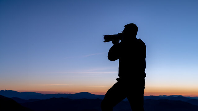 The silhouette of a tourist taking a photo at the top of the mountain