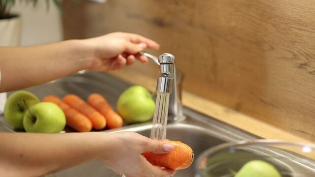 Side view of woman wash carrots. Preparing fruits and vegetables for healthy homemade juice