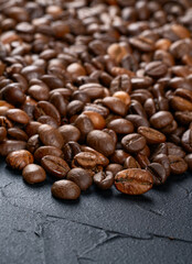 Scattered roasted coffee beans by a large pan on a dark background