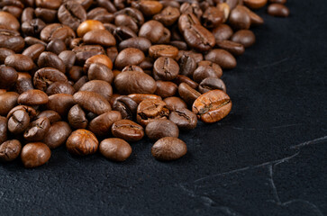 Scattered roasted coffee beans by a large pan on a dark background