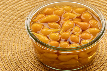 Pickled whole Biquinho Yellow chili in a glass jar on a yellow background. Sour and sweet Asian-style pickled homegrown chilies.