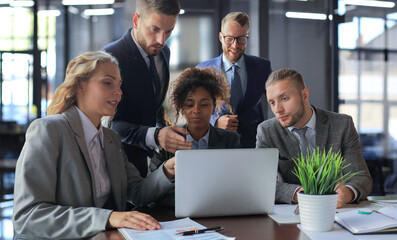 Group of young modern people in formalwear smiling and discussing something while working in the modern office