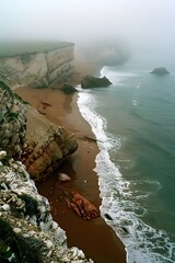 Aerial shot of Alslot de la Torre's foggy coastline, showcasing the deformed palette rocks, brown sand, and lush greenery, captured with a Canon EOS.