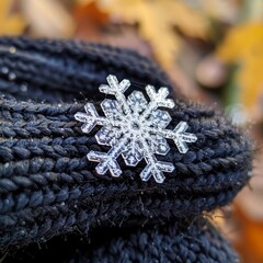 Close-up of a glittering snowflake decoration resting on the woven pattern of a black knitted fabric.