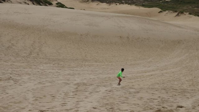 Young boy sandboarding down dune hill in front of beach on summer day - visualization success