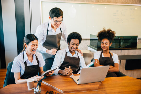 At their stylish coffee shop diverse entrepreneurs hold a team meeting. Barista and owner discuss work on laptop. Multiethnic employees successful teamwork business discussion.