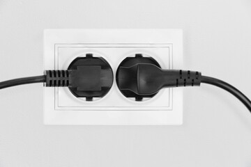 Power electric sockets on a white wall. electric cord plugged into a white electricity rosette on...
