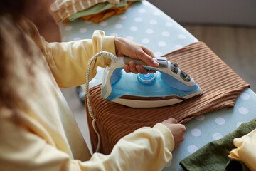 High angle closeup of unrecognizable woman ironing clothes with cute light blue iron appliance at...