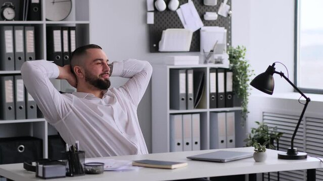 Caucasian businessman celebrating successful deal, relaxing at workplace in office. Rejoicing ending of a workday or week. In anticipation of weekend.