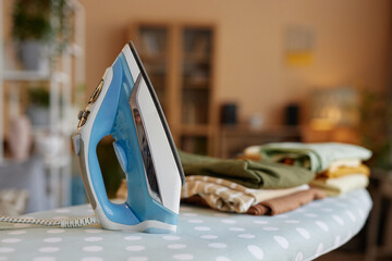 Close up background image of light blue iron on ironing board with stack of clothes copy space