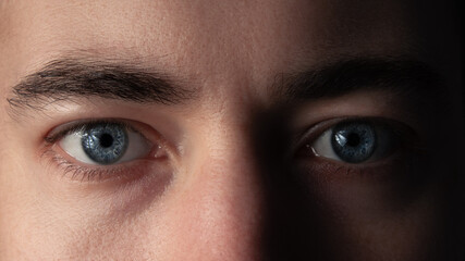 Blue eyes of a young man in dramatic lighting, close-up