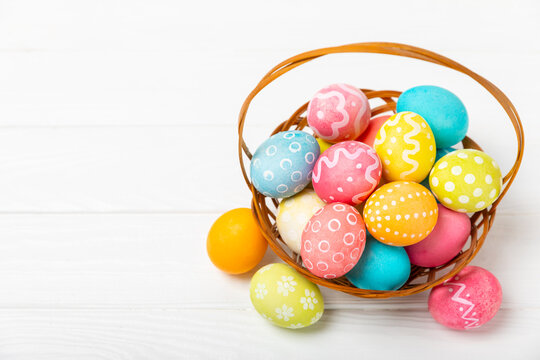 Easter basket filled with colorful eggs and a bouquet of tulips on a textured wooden table. Easter celebration concept. Colorful easter handmade decorated Easter eggs. Place for text. Copy space