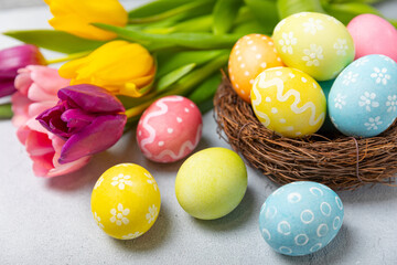 Fototapeta na wymiar Easter eggs in the nest with mimosa flowers on a bright background. Easter celebration concept. Colorful easter handmade decorated Easter eggs. Place for text. Copy space.