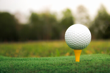Golf ball set on yellow tee, blurred background and warm light.