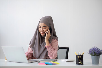Smiling Muslim business woman Wearing a hijab while chatting online on a work desk in the office.
